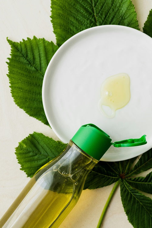 An oil bottle spilling on a plate with a leaf in the background