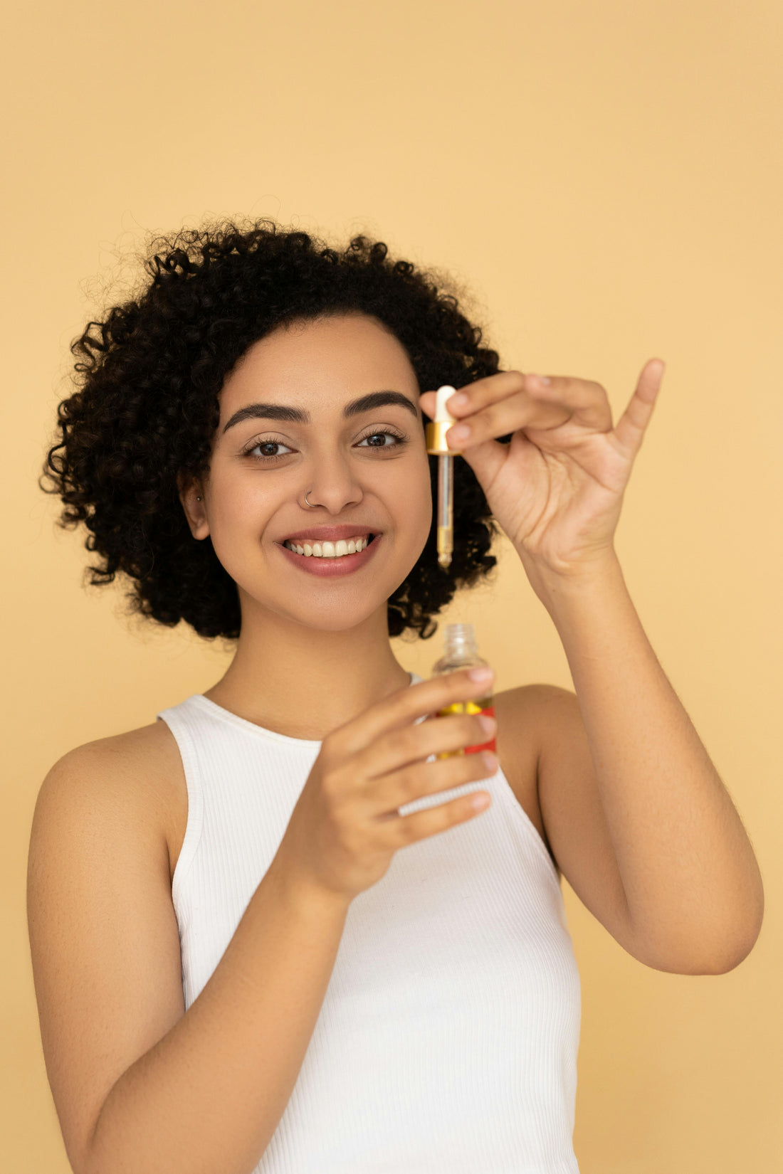 A curly haired woman showcasing a glass dropper bottle with oil 